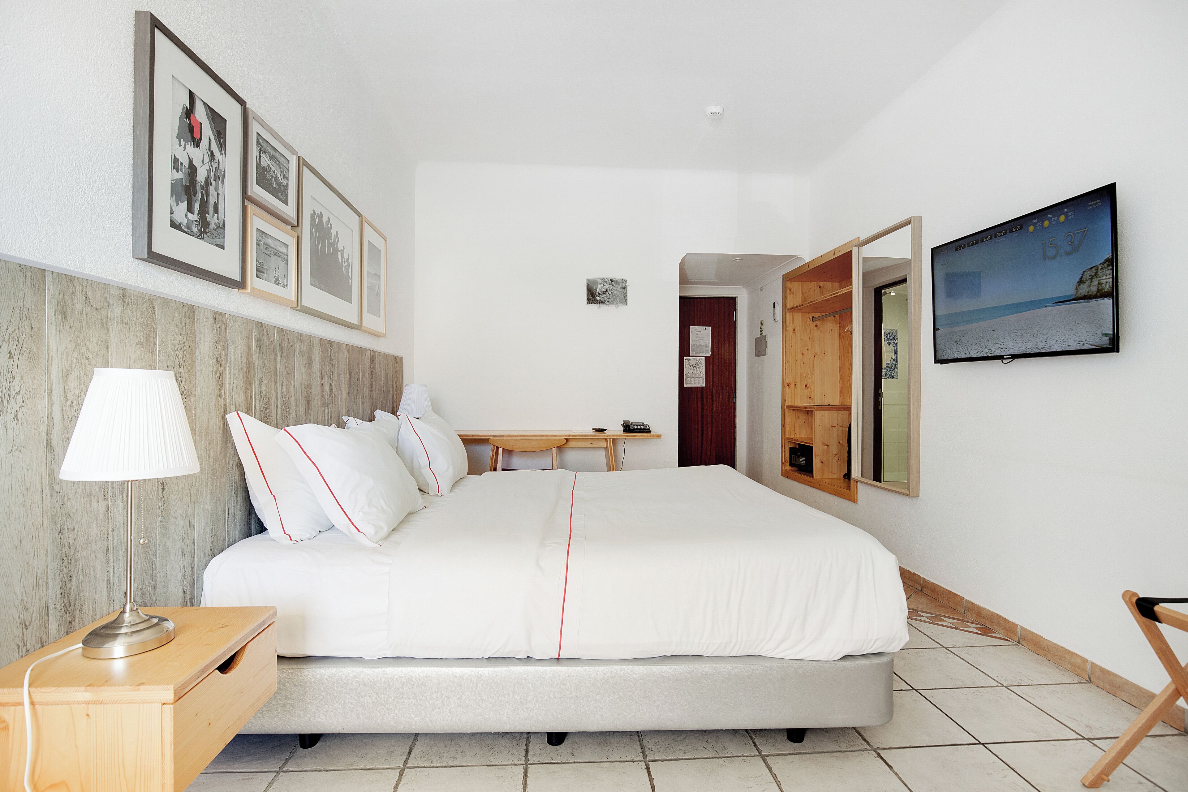 Una habitación de hotel con una cama, una mesita de noche, una lámpara y un televisor en la pared.