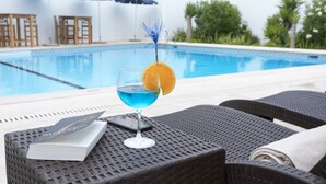 Een zwembadterras met een drankje, een boek en ligstoelen.