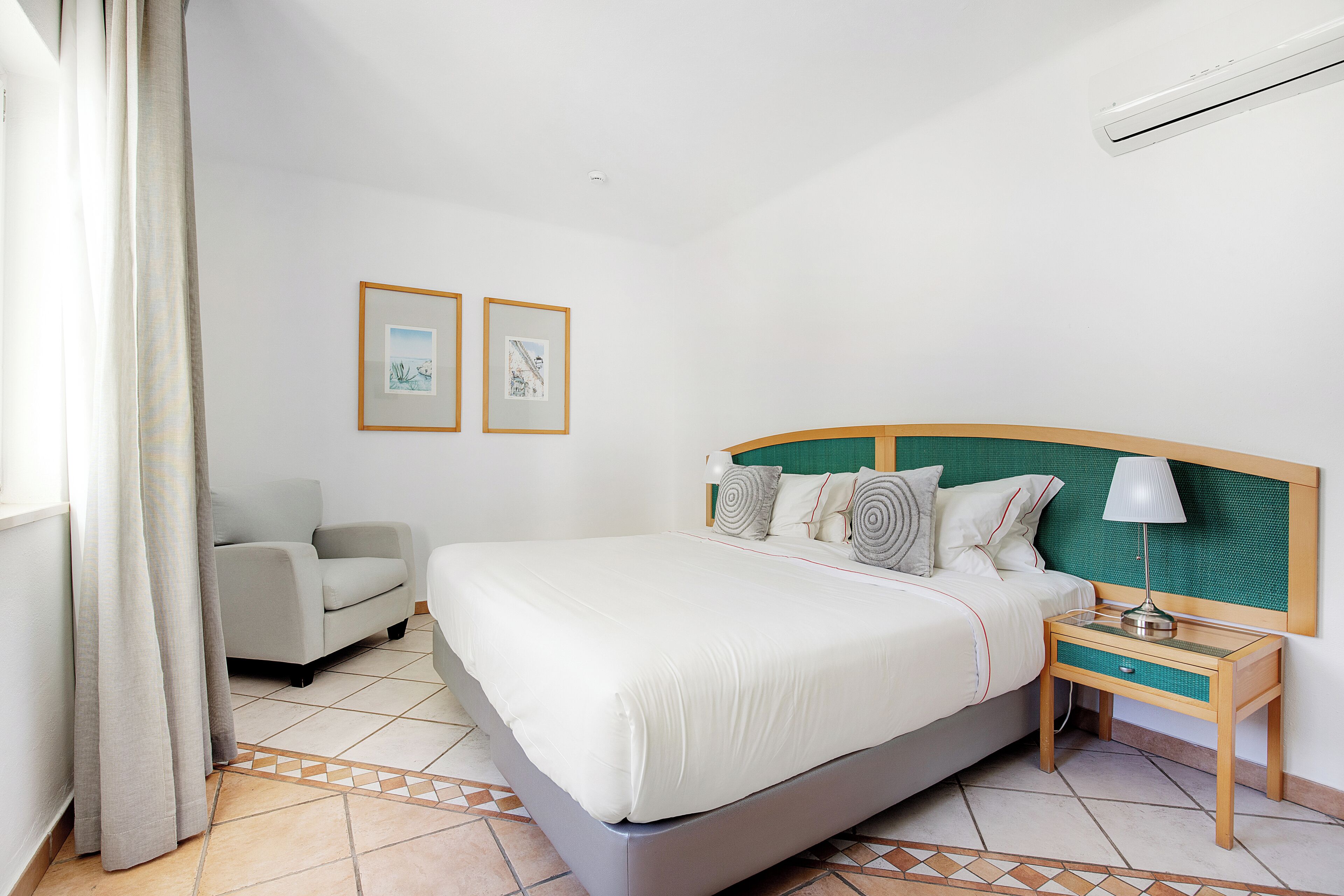 Habitació d'hotel amb un llit, una taula de nit, una cadira i dues imatges emmarcades a la paret.