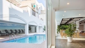 A modern indoor swimming pool with lounge chairs, a wooden deck, and a view of the surrounding buildings. - Planet Hotels One Adults Only +16 (Palma de Mallorca)
