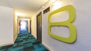 A hotel hallway with a checkered carpet, a large illuminated number '8' on the wall, and a door with a sign above it. - Globales Honolulu (Calvia)