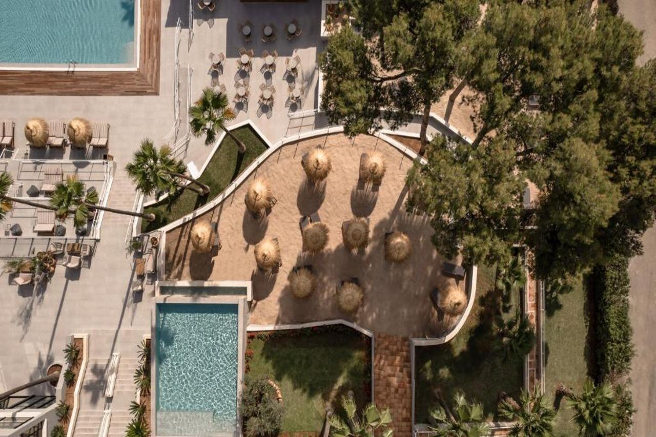 An aerial view of a resort with a pool, sun loungers, and a circular seating area with thatched umbrellas.