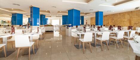 A spacious dining area with white tables and chairs, blue accent columns, and a polished tile floor.