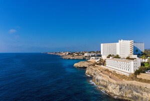 Un hotel frente al mar con varias plantas, un litoral rocoso y una vista despejada del océano.