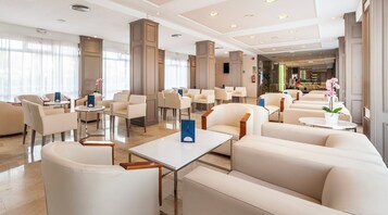 Un vestíbulo de hotel con zonas de estar, una recepción y vistas al restaurante.