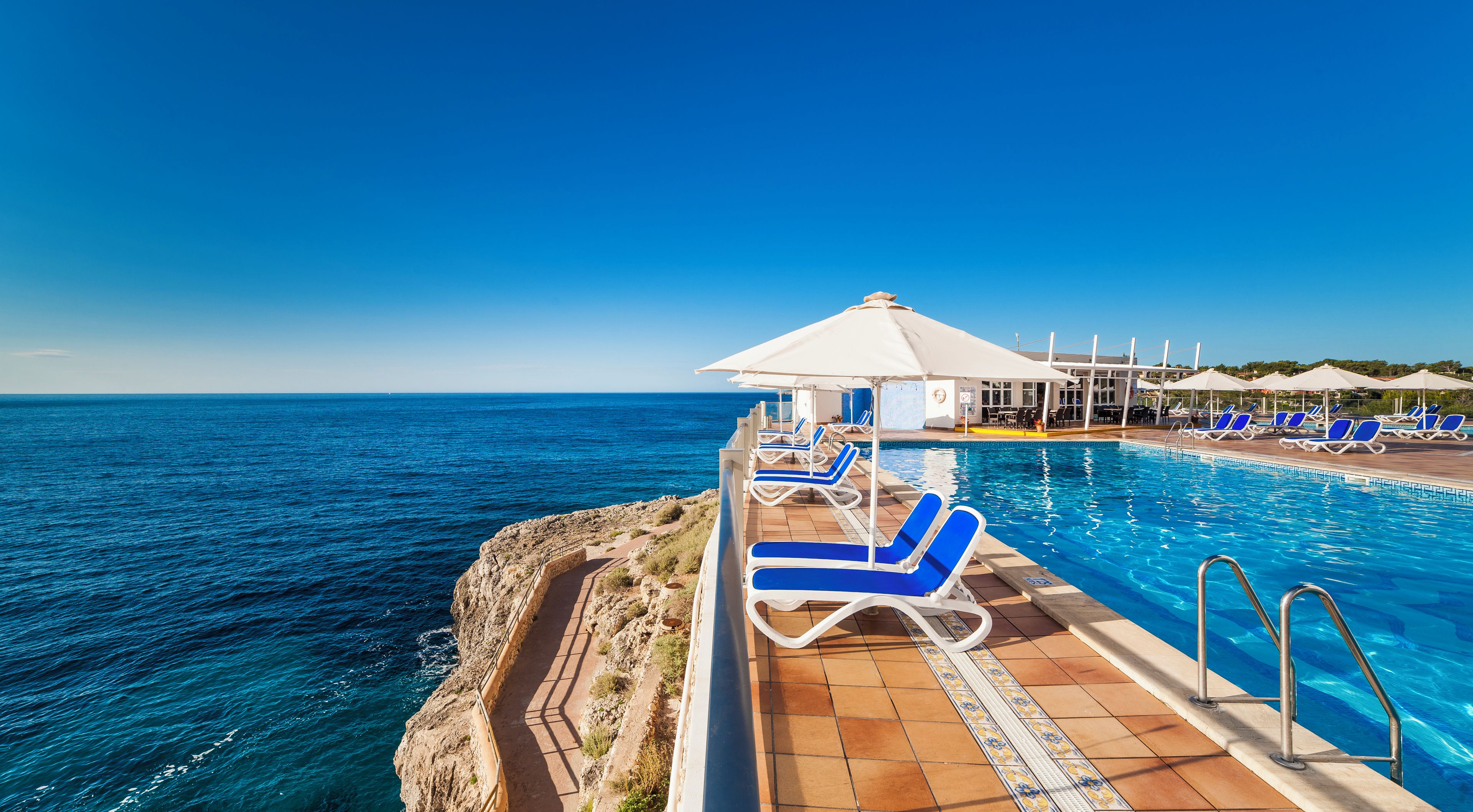 A poolside area with lounge chairs and umbrellas overlooking a body of water.