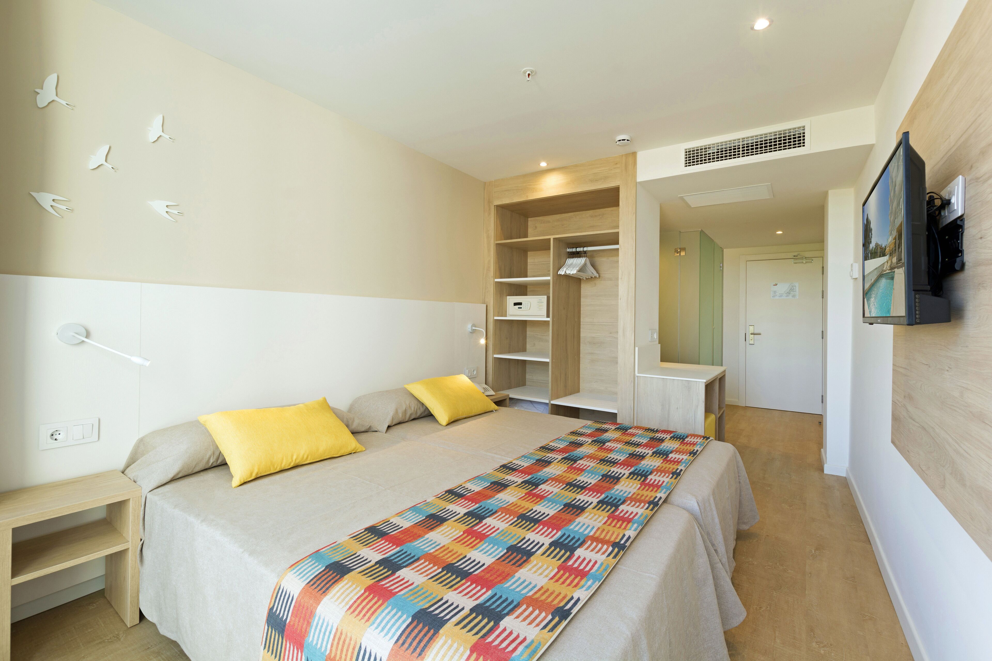 Una habitación de hotel con cama, mesita de noche, armario y televisor montado en la pared.