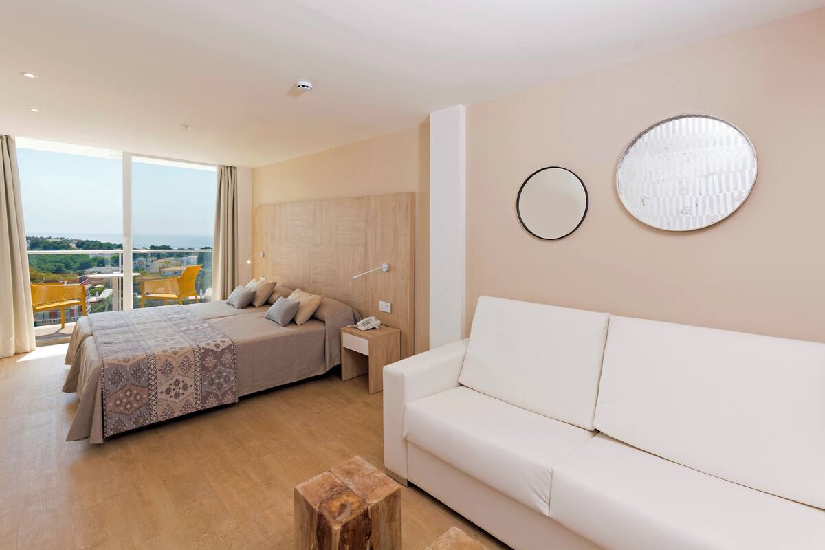 Ein modernes Schlafzimmer mit einem großen Bett, einem weißen Sofa und einem Balkon mit gelben Stühlen.