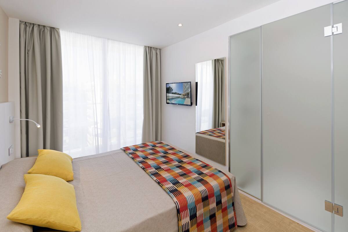 Ein modernes Hotelzimmer mit einem großen Bett, einem an der Wand befestigten Fernseher und einem Schiebetürenschrank.
