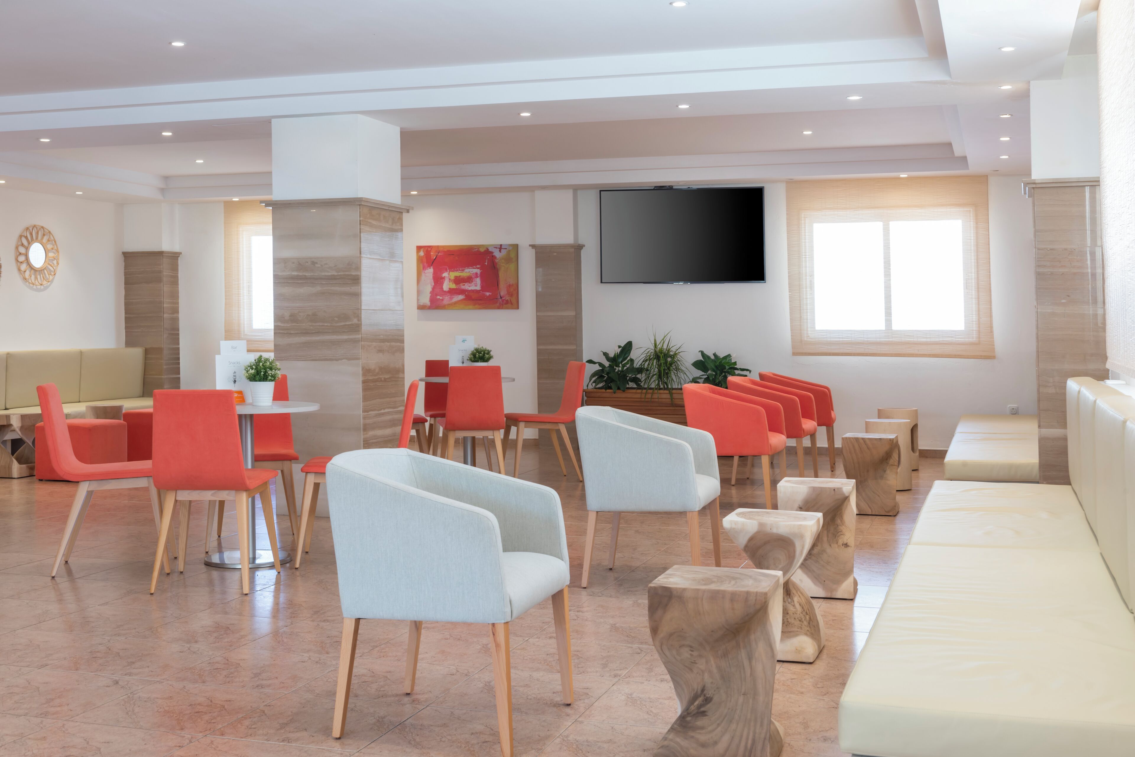 A modern hotel lobby with seating areas, a flat-screen TV, and a large window.