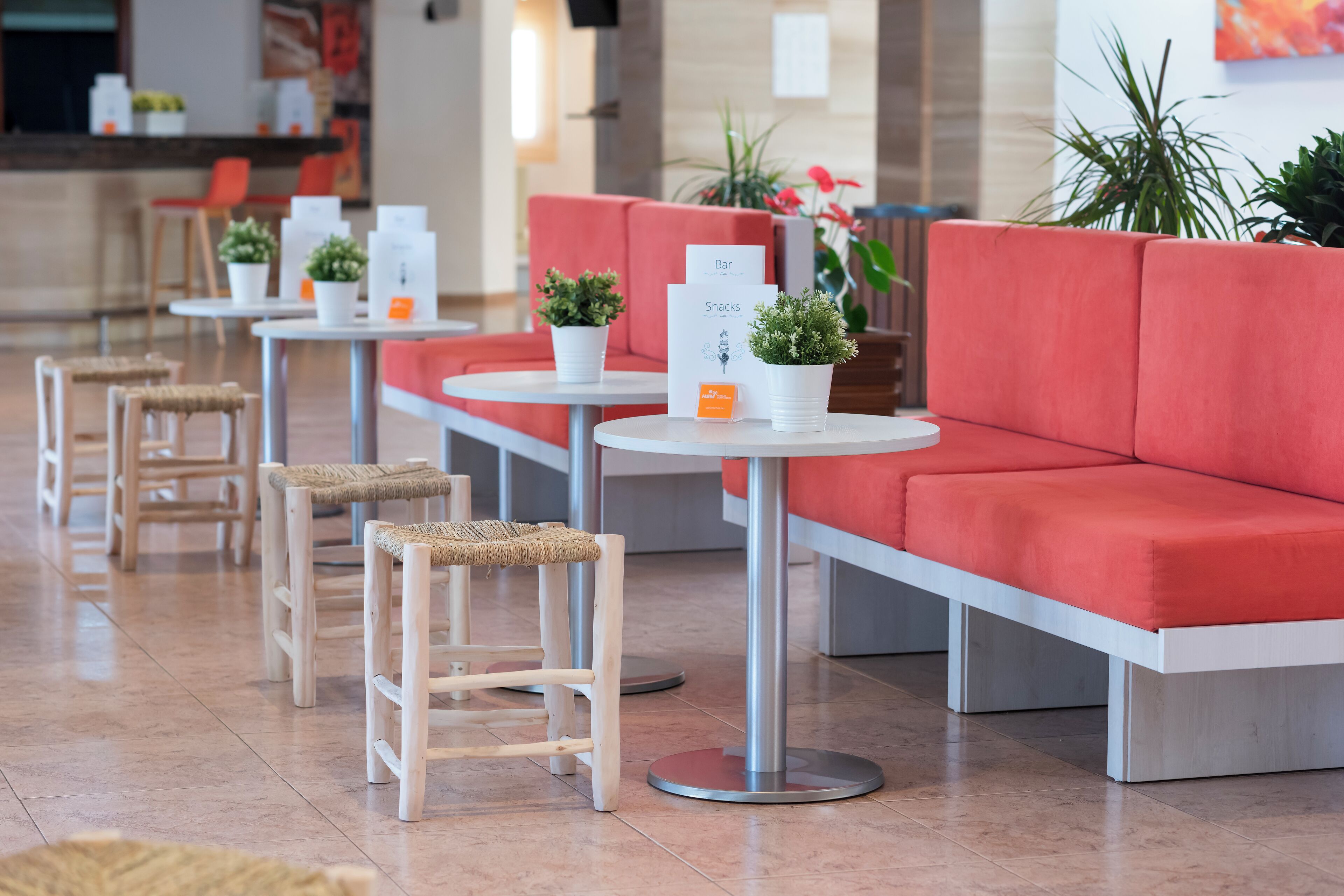 Un moderno vestíbulo de hotel con asientos rojos, mesas redondas y plantas en macetas.