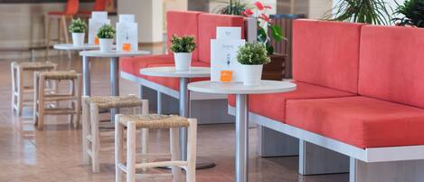 Un moderno vestíbulo de hotel con asientos rojos, mesas redondas y plantas en macetas.