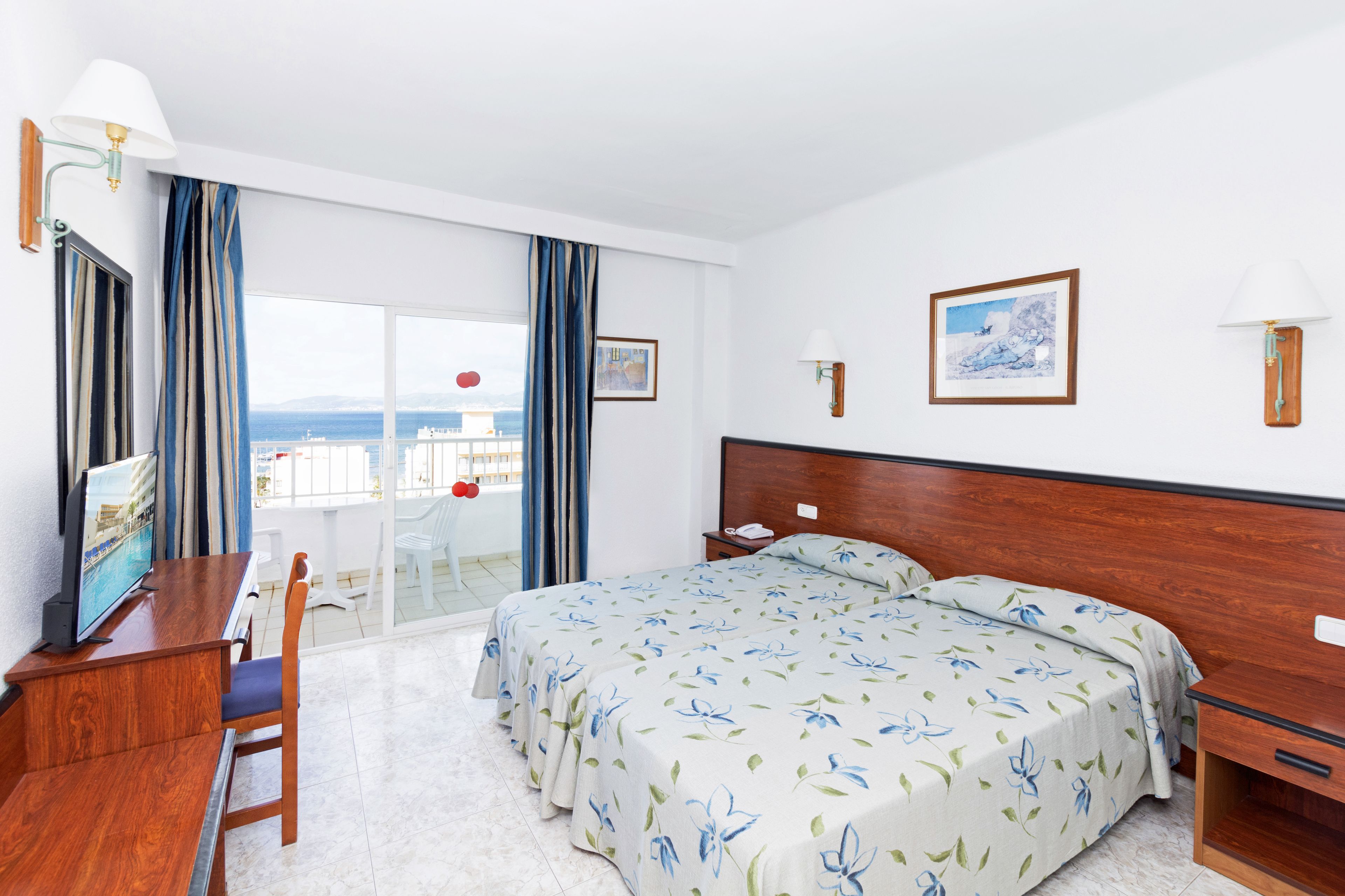 A hotel room with a large bed, a desk, a chair, and a view of the sea.