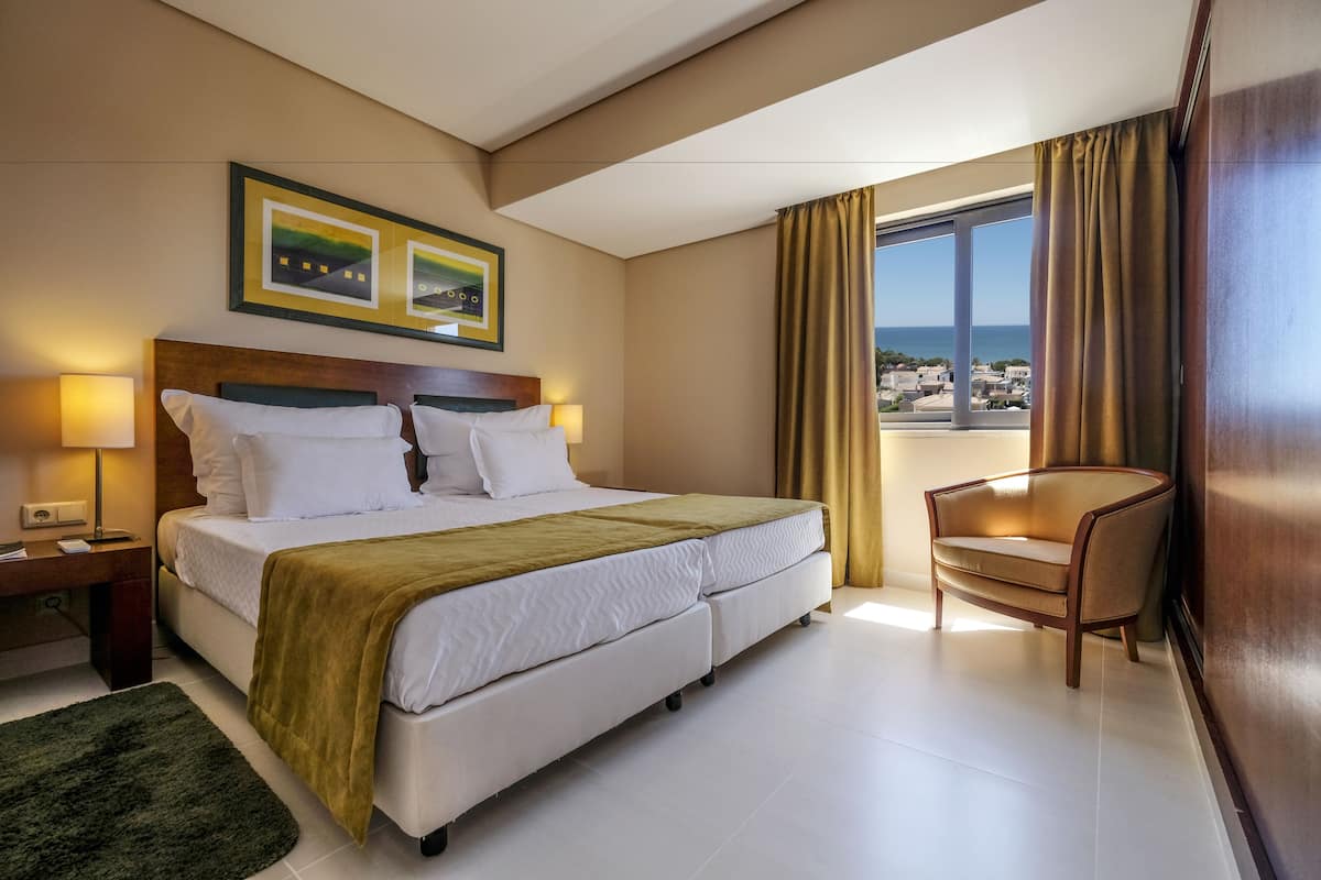 A hotel room with a bed, bedside table, lamp, chair, and a window with curtains.