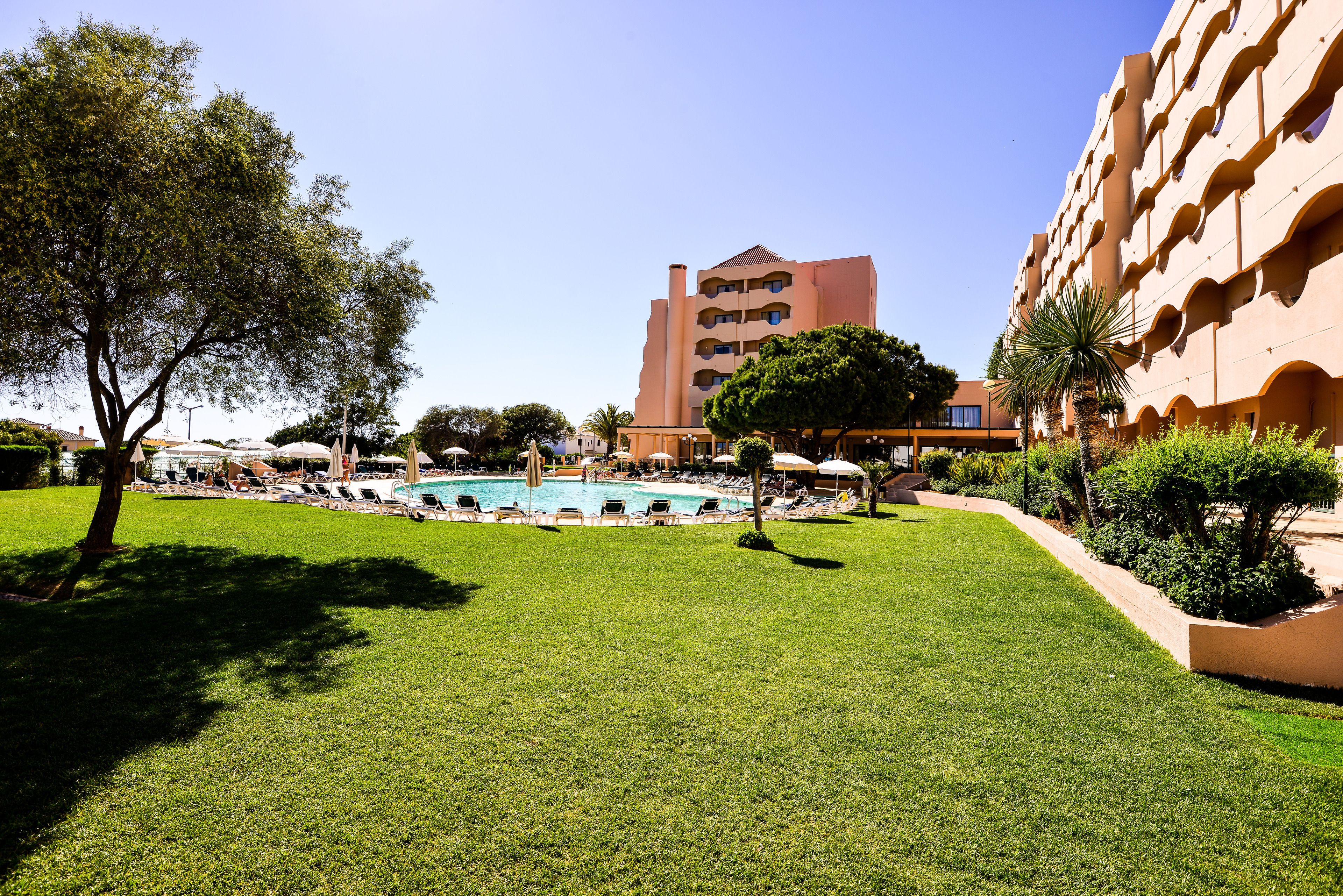 Un hôtel doté d’une piscine, entouré de pelouses bien entretenues et de palmiers.