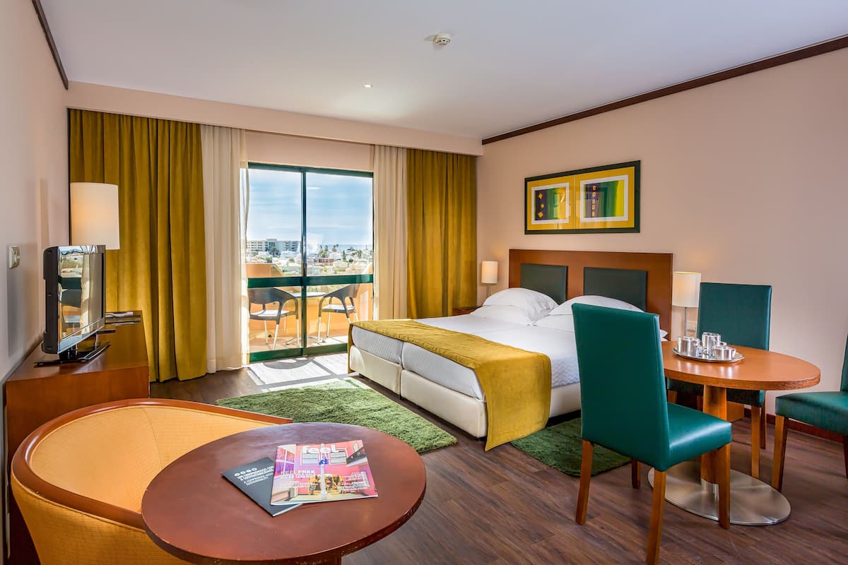 A hotel room with a bed, a desk, a chair, a table, a TV, and a view of the city.