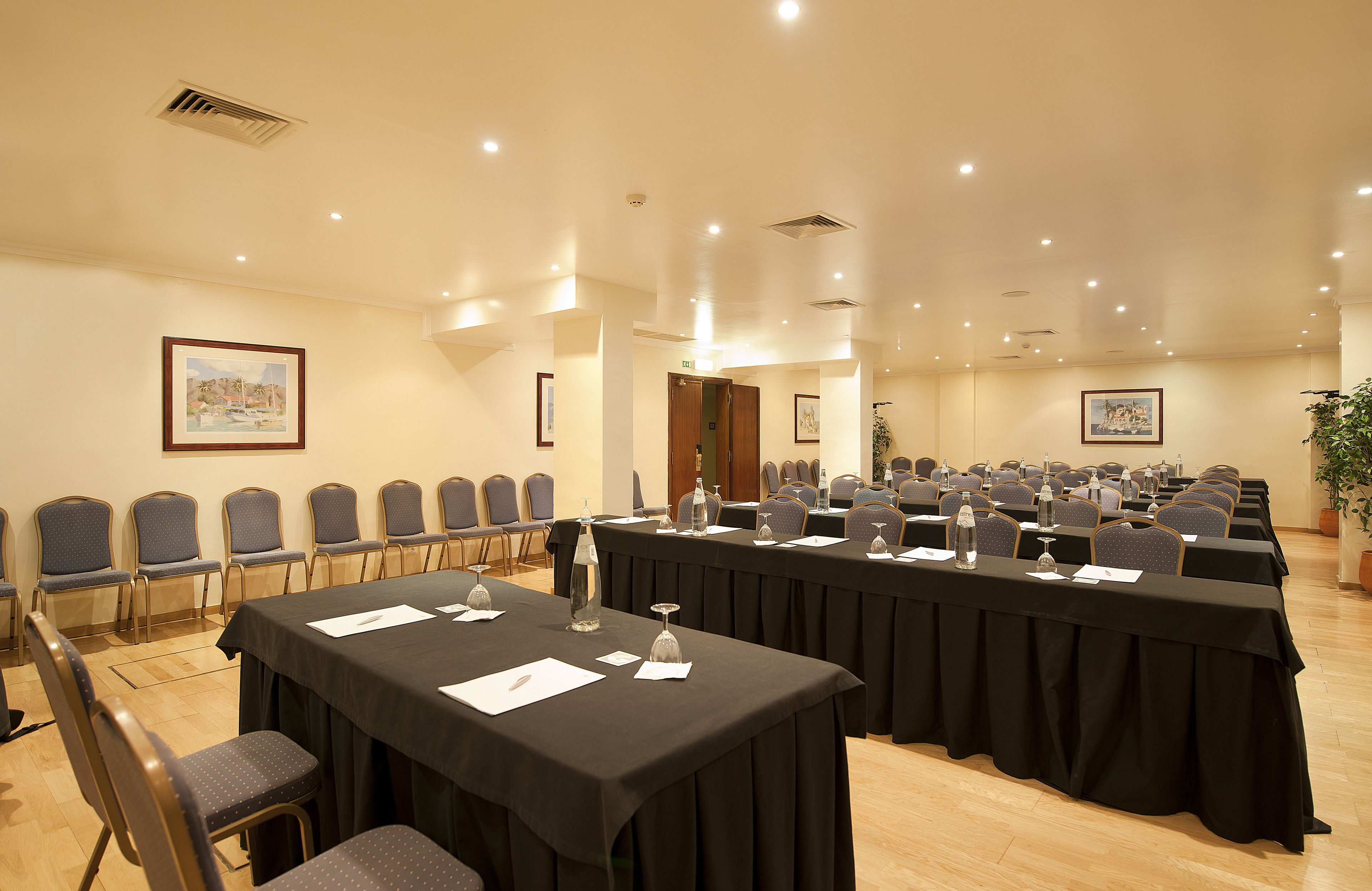 A conference room with multiple tables and chairs, equipped with water bottles and papers.