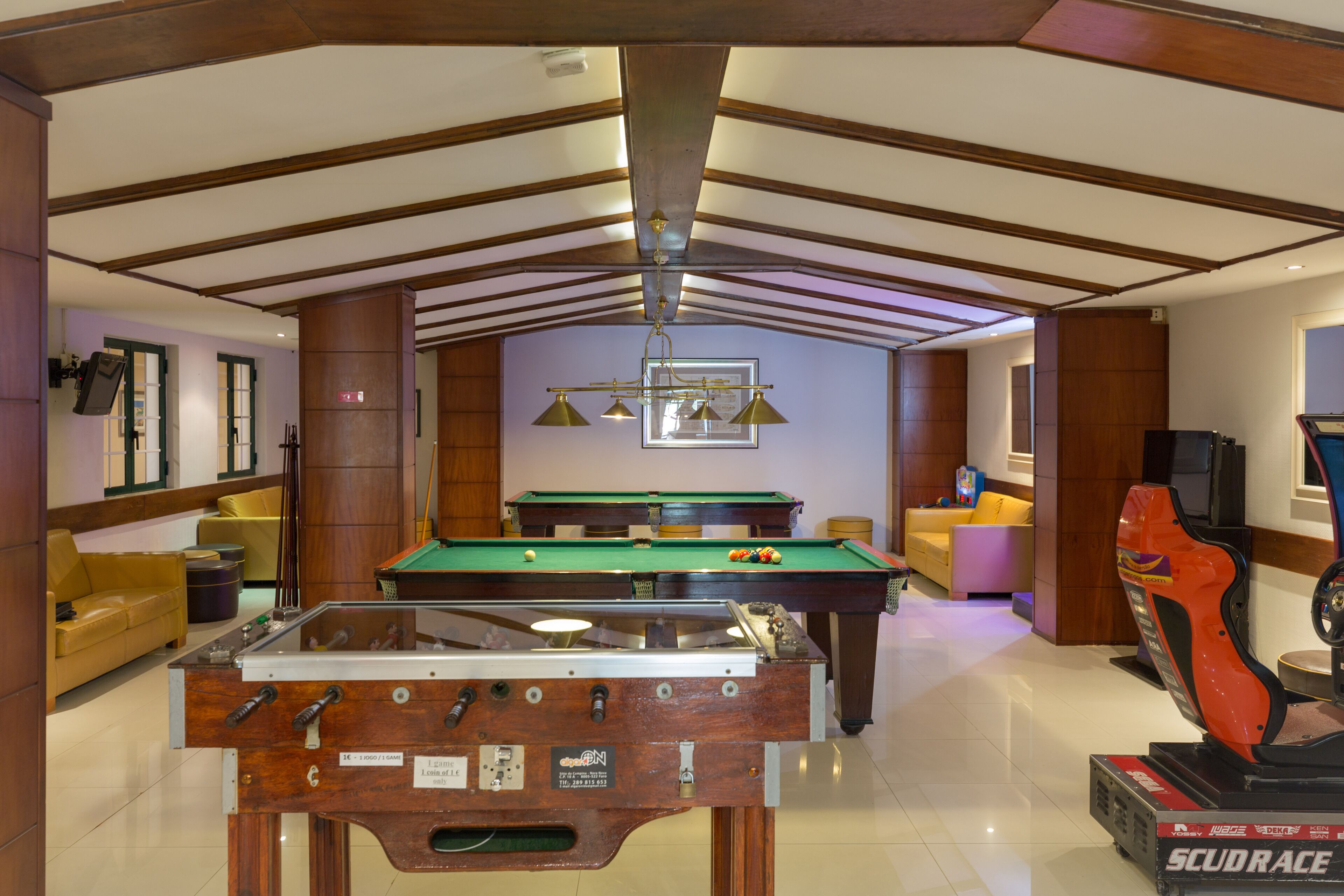 A spacious indoor area with a foosball table, pool table, and a racing simulator.