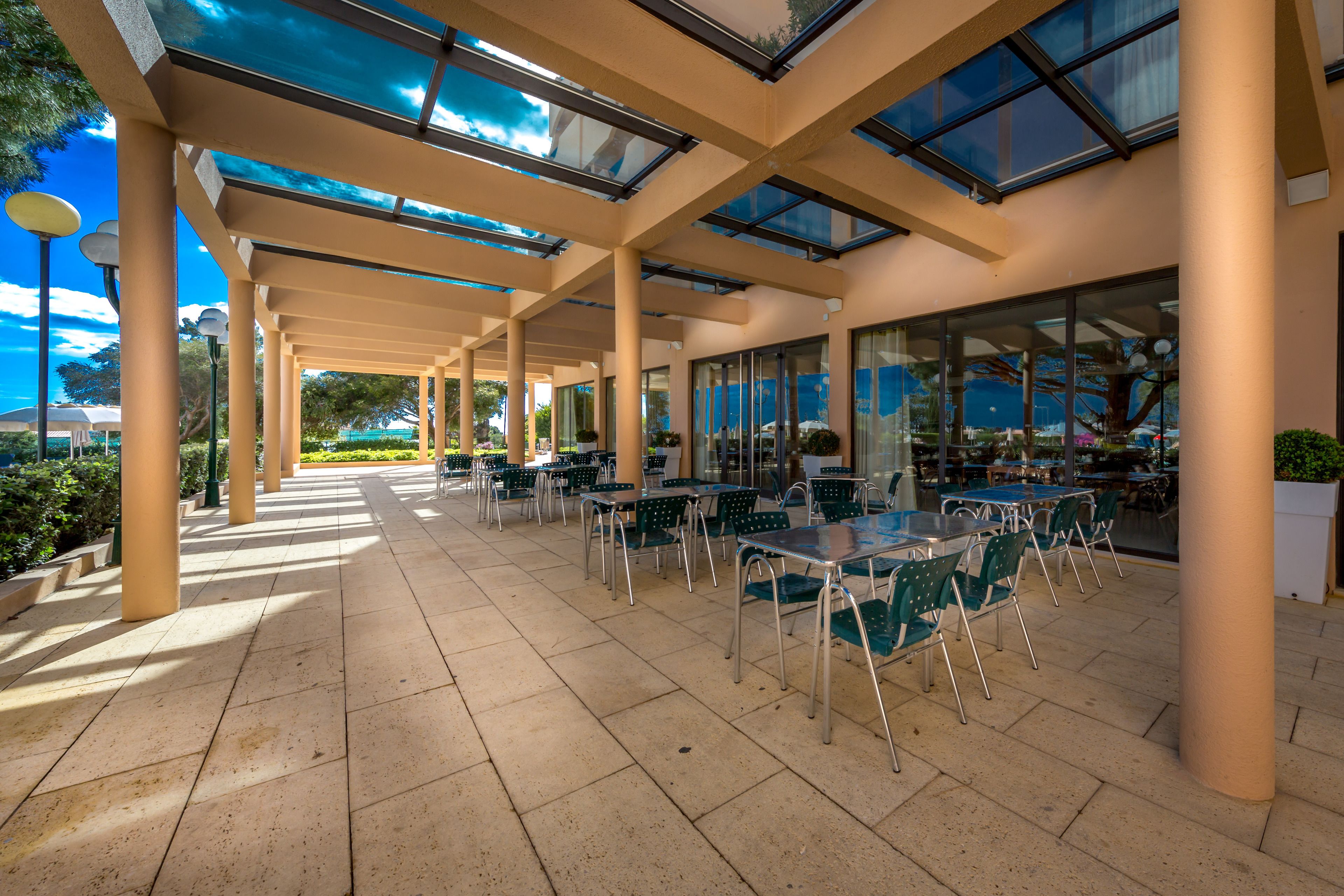 An outdoor patio area with tables and chairs, a glass ceiling, and a view of the surrounding landscape.