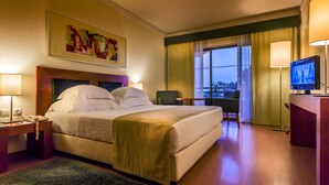 Habitación de hotel con cama, mesitas de noche, un escritorio con silla, televisor y un ventanal con cortinas.