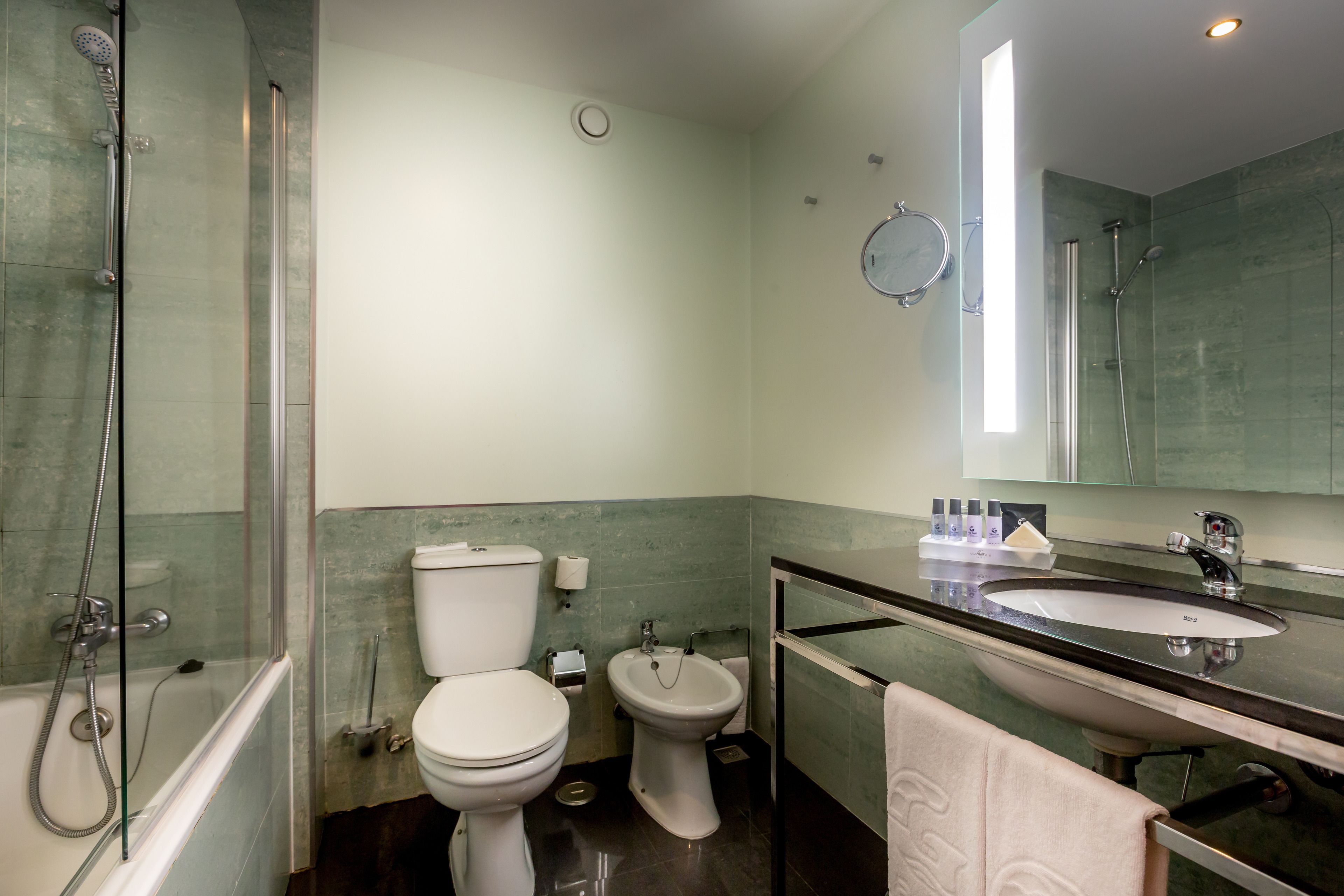 Un baño moderno con bañera, inodoro, bidé y lavabo con espejo superior.