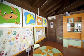 Ein Klassenzimmer mit Lehrmaterialien, einem Bulletin Board mit Kinderarbeiten und einem kleinen Tisch mit buntem Design.