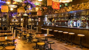 Un bar con mesas y taburetes de madera, una barra con botellas y bolas de discoteca colgantes.