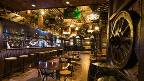 Un área de bar con mesas y taburetes de madera, una noria grande y varias decoraciones colgantes.