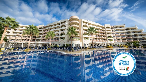 Un hotel con una piscina amplia, varios balcones y palmeras.