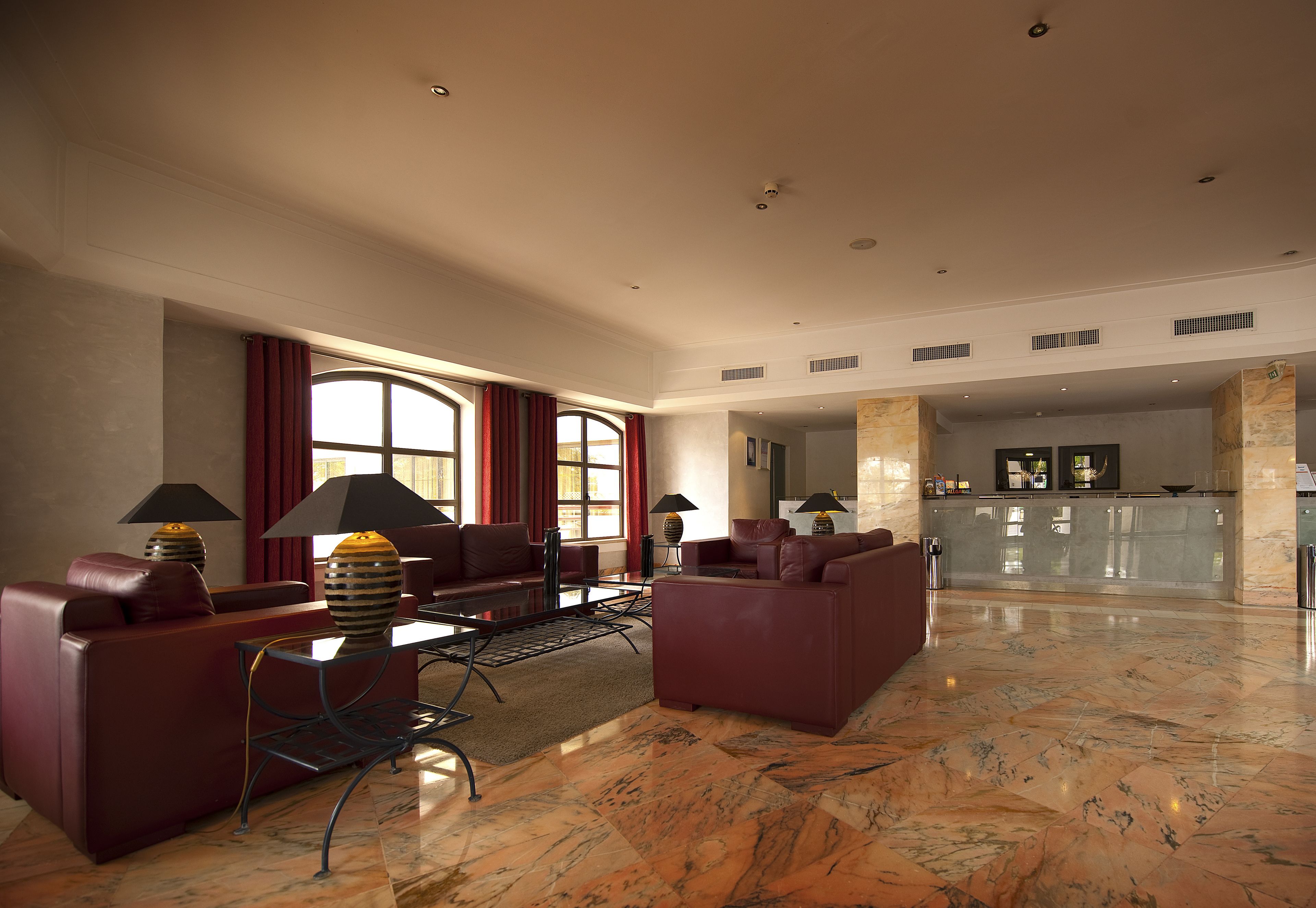 A spacious living area with leather sofas, a coffee table, and lamps. A kitchen area is visible in the background.