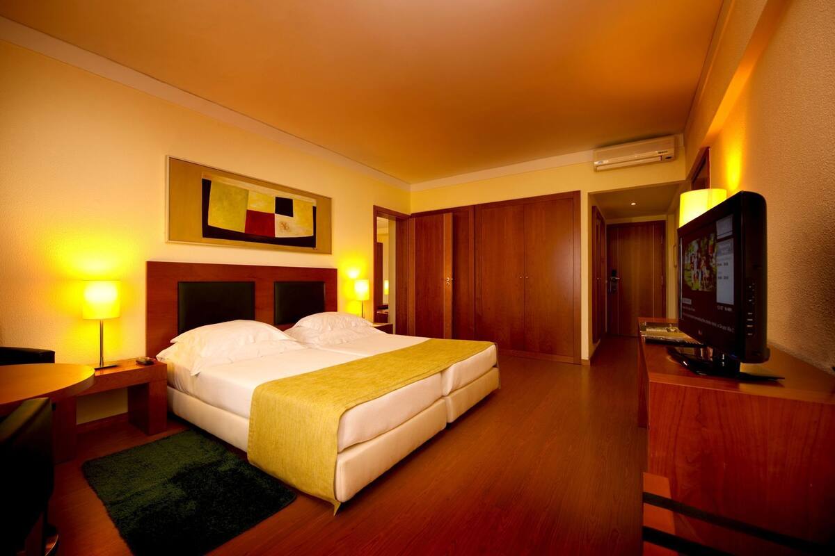A hotel room with a bed, bedside lamps, a television, and a wooden wardrobe.