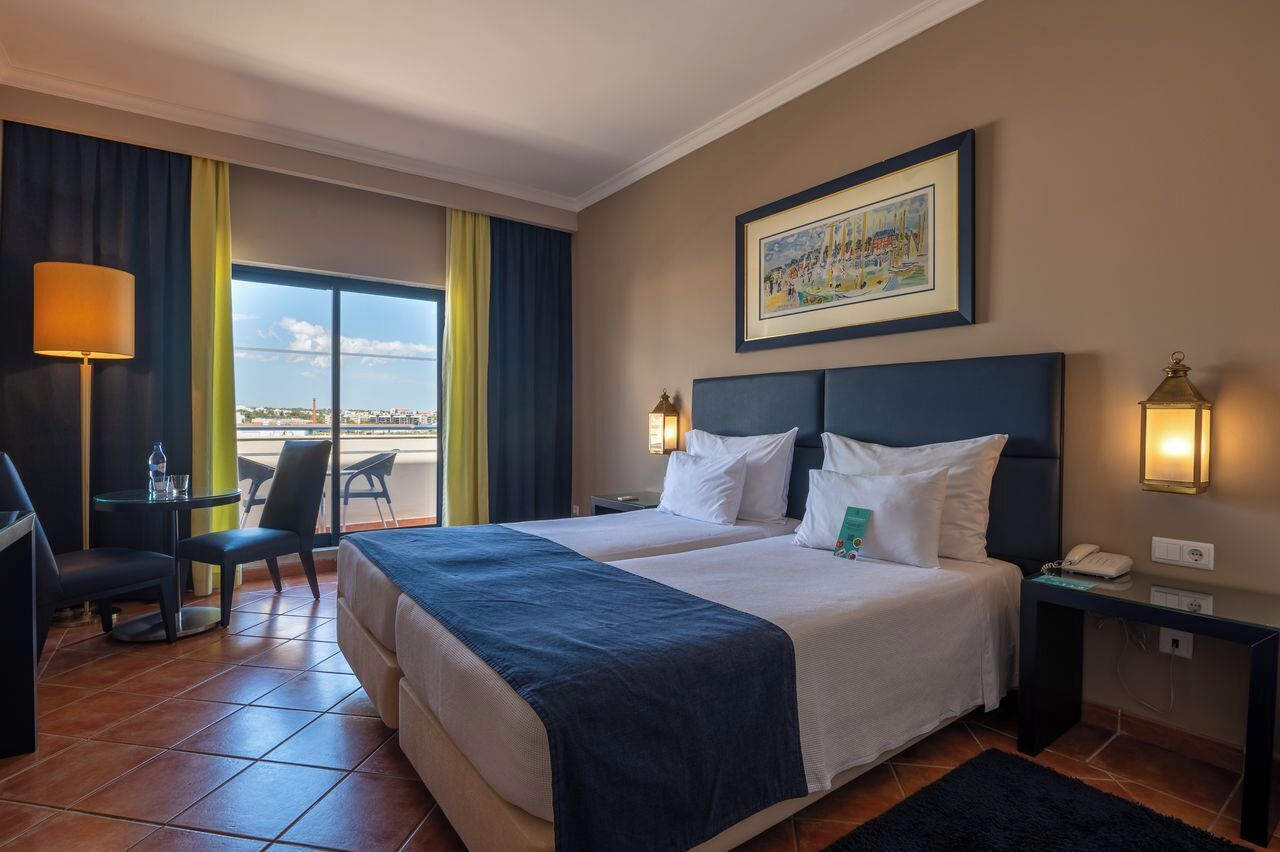 Een hotelkamer met twee bedden, een bureau met stoel, een lamp en een schilderij aan de muur.