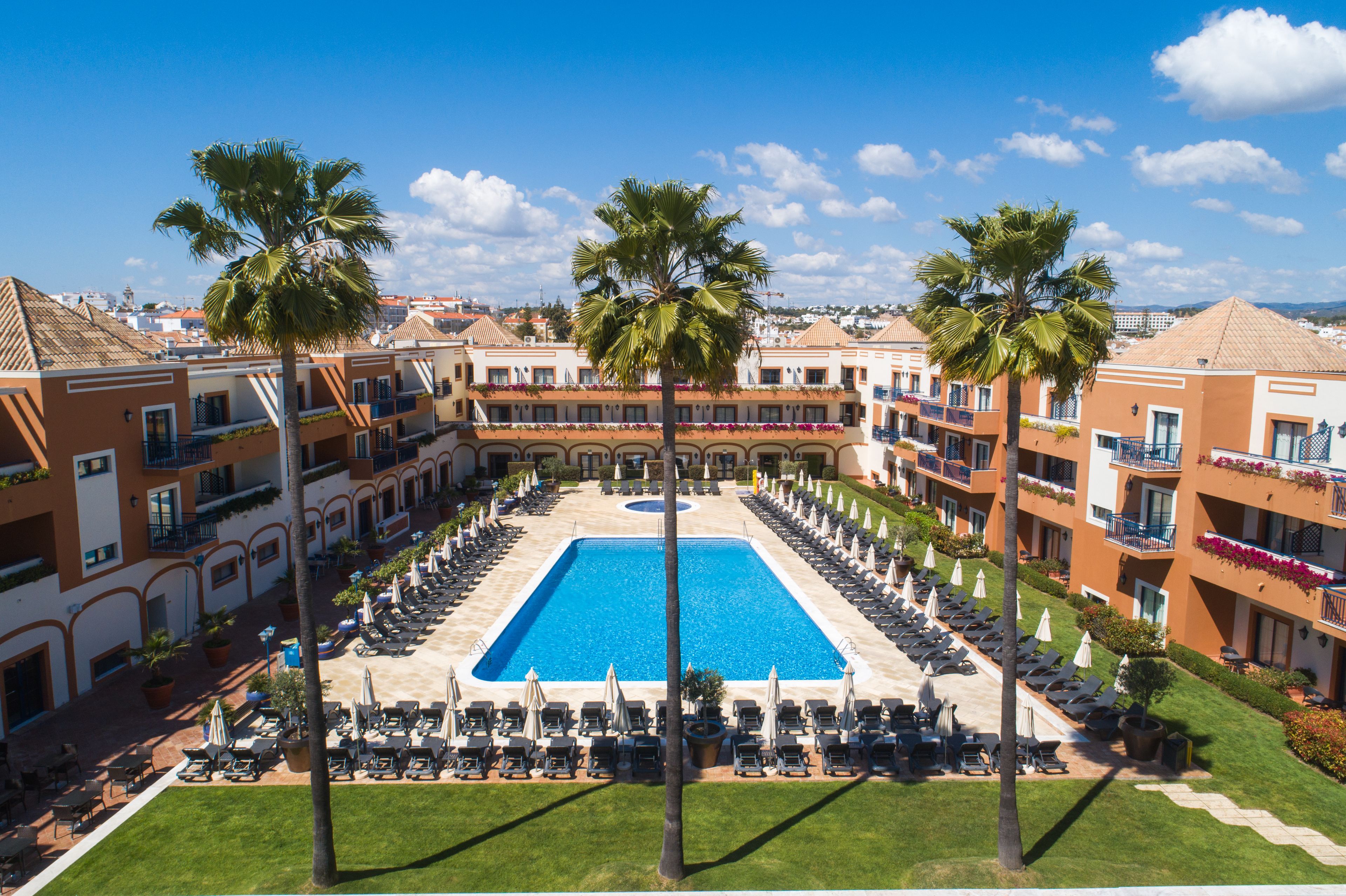Un hôtel doté d’une piscine centrale, entourée de transats et de palmiers.