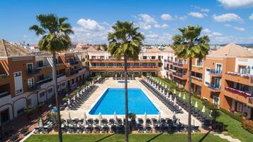 Un hôtel doté d’une piscine centrale, entourée de transats et de palmiers.