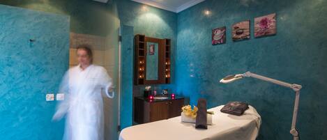 Une salle de spa équipée d’une table de massage, d’une coiffeuse avec un miroir et d’un mur décoré d’œuvres d’art florales.