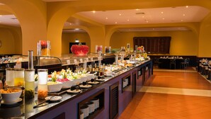 A buffet with various food items and beverages, a large decorative fruit bowl, and a seating area with tables and chairs.