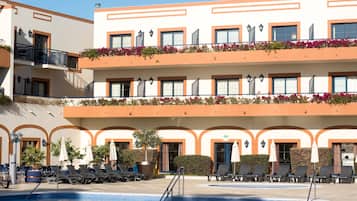 A hotel with a pool area, multiple balconies with flowers, and outdoor seating.