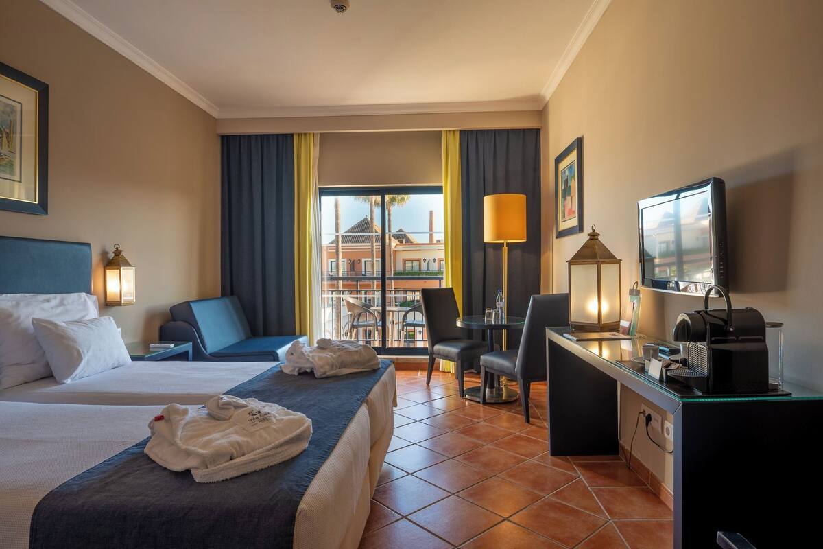Une chambre d’hôtel avec deux lits, un bureau, une chaise, une télévision et un balcon avec vue.
