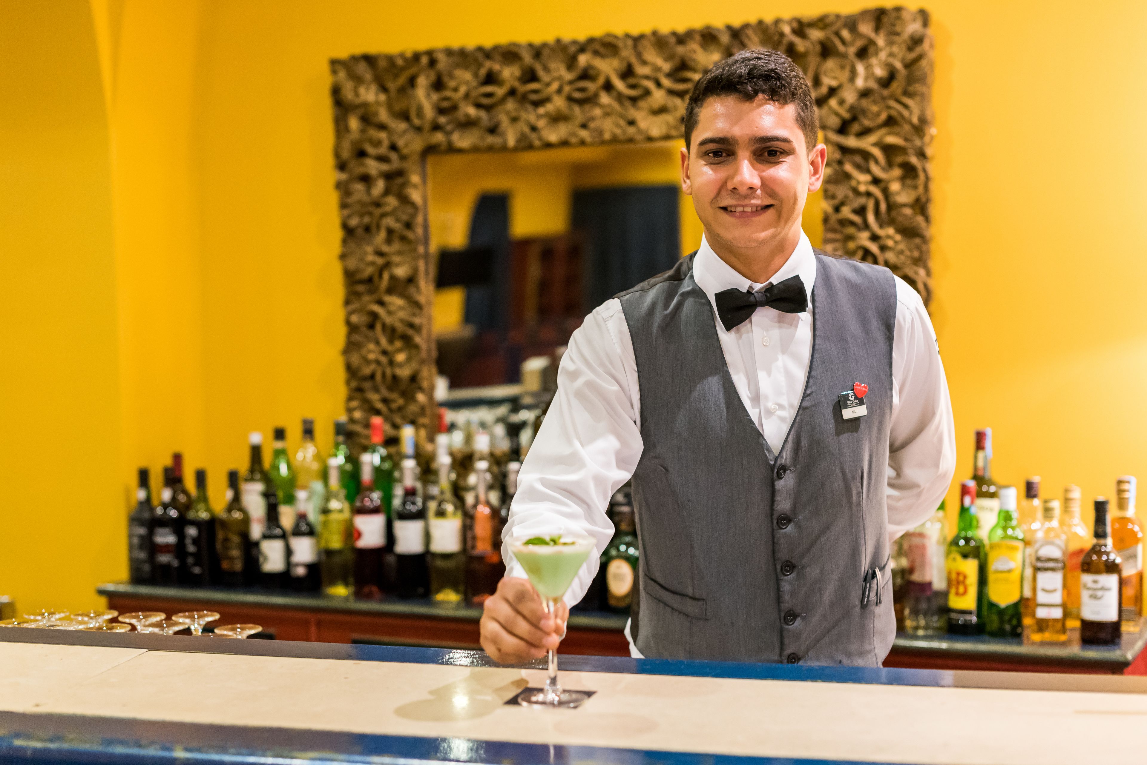 A bartender in a formal uniform holding a cocktail glass.