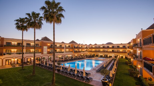 A hotel courtyard with a swimming pool, lounge chairs, and palm trees.