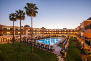 Une cour d’hôtel avec une piscine, des chaises longues et des palmiers.