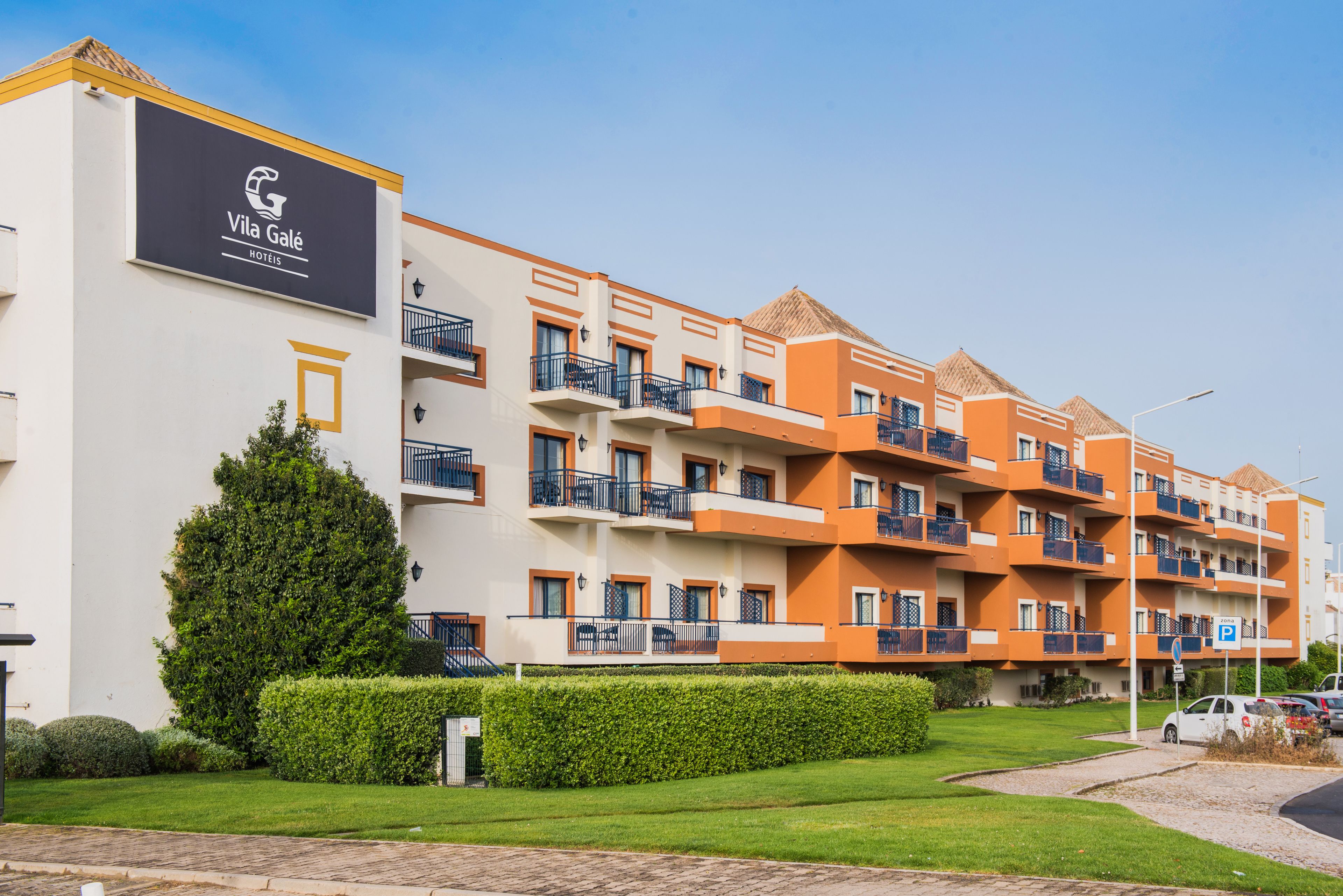 A multi-story hotel with balconies, a parking sign, and a well-maintained lawn.