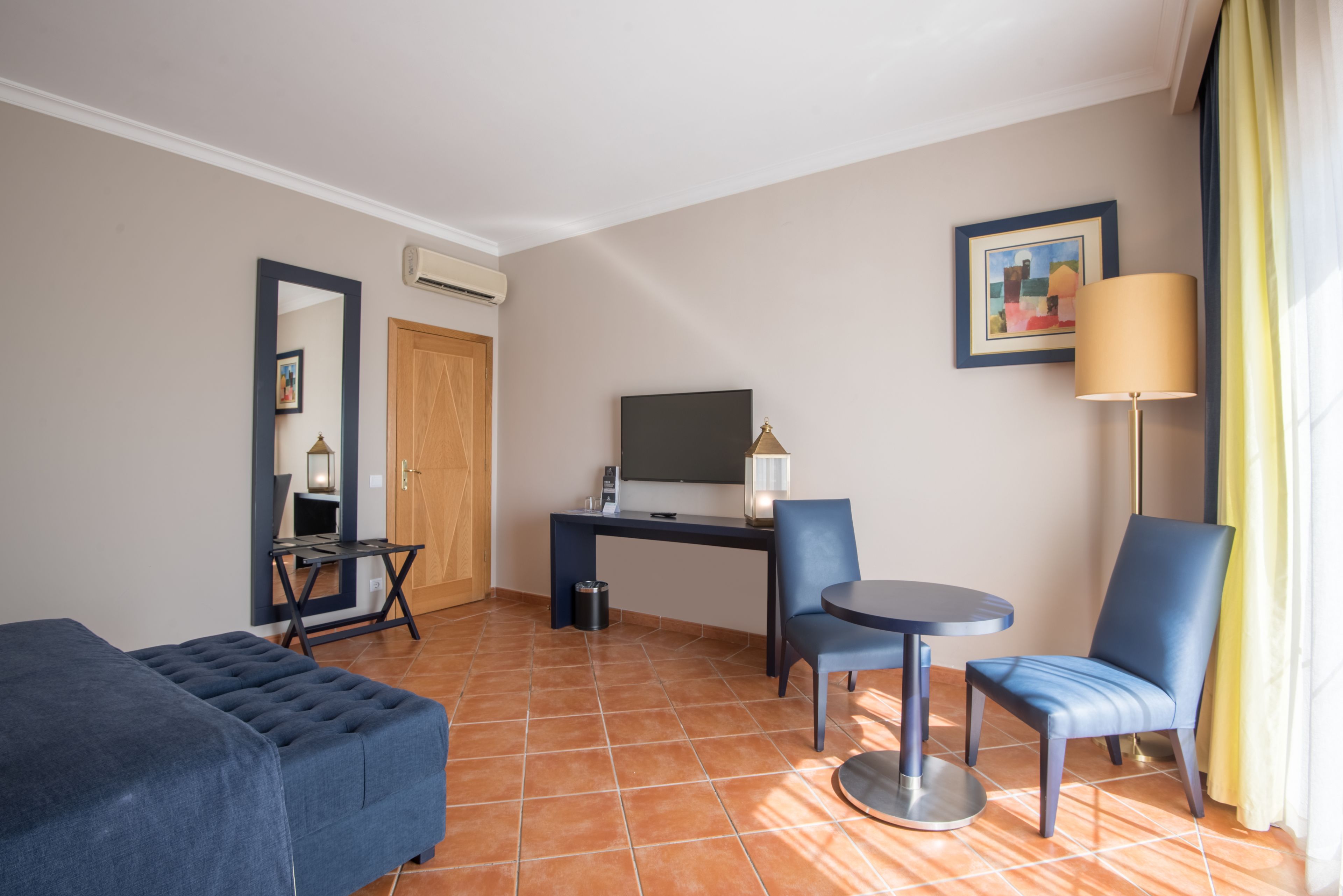 Ein Hotelzimmer mit einem Bett, einem Schreibtisch mit Computer, einem Stuhl, einem kleinen Tisch und einer Lampe.