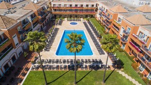 A hotel with a central swimming pool surrounded by lounge chairs and palm trees.