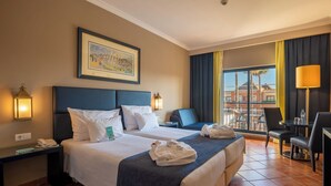 A hotel room with two beds, a desk, a chair, a table, and a view of the city.