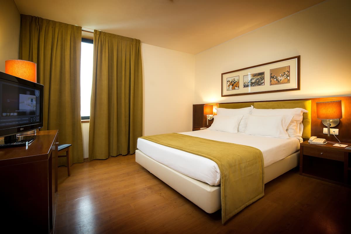 A hotel room with a bed, a television, a desk, and a window with curtains.