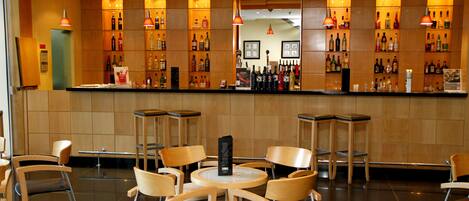 Un área de bar con diversas opciones de asientos, incluyendo mesas redondas y sillas, y estantes llenos de diferentes botellas.