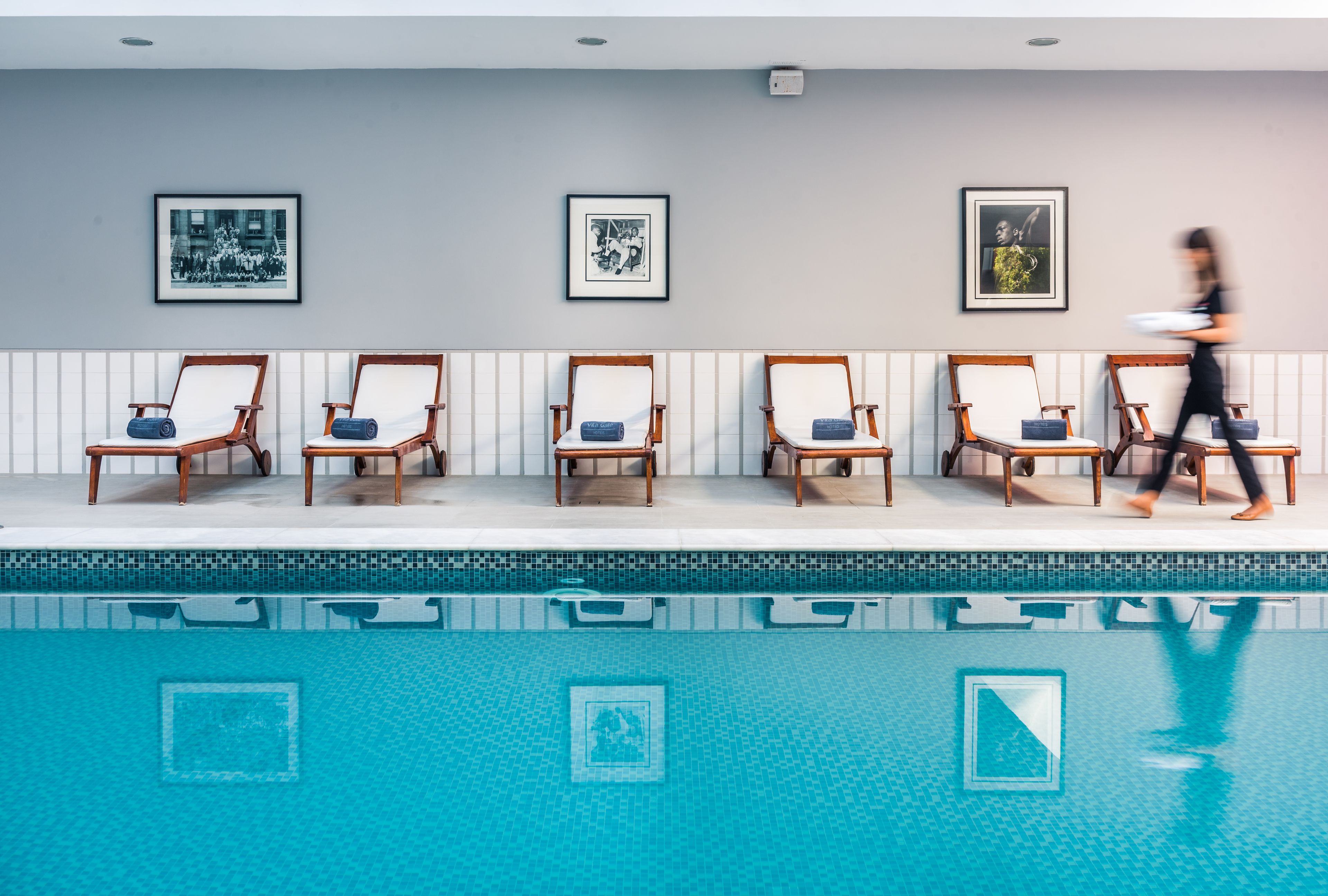 Un espace aménagé au bord de la piscine, avec six chaises longues disposées en rangée contre un mur, et trois tableaux encadrés accrochés à ce mur.