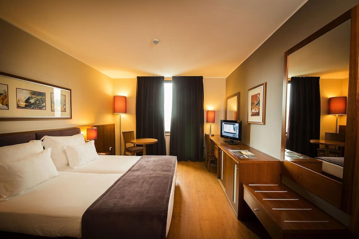 A hotel room with a bed, desk, chair, TV, and artwork on the walls.