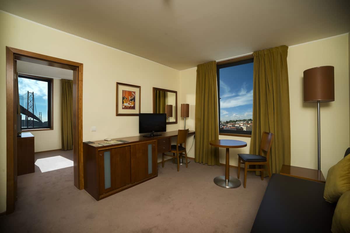 A hotel room with a desk, television, and a view of a bridge.